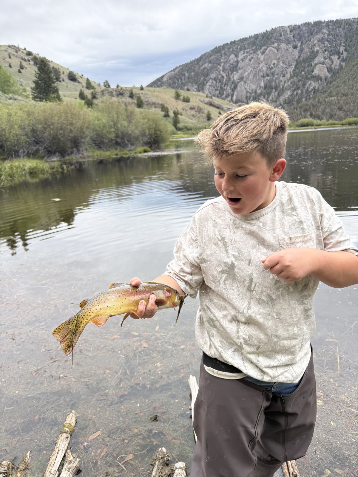 Caden looking amazed holding a brown trout beside a mountain lake