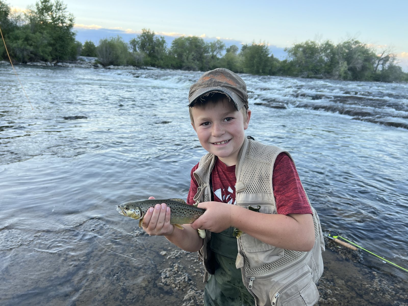 Caden standing in a river at sunset holding a brown trout