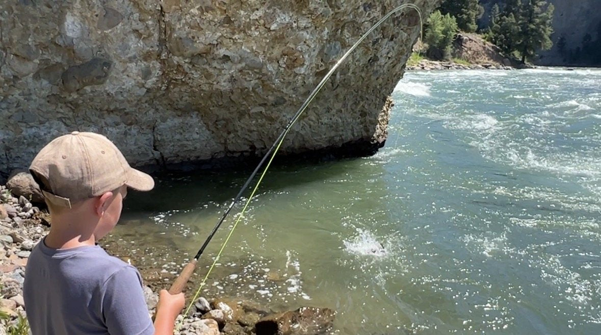Young Caden casting a fly rod beside a fast river